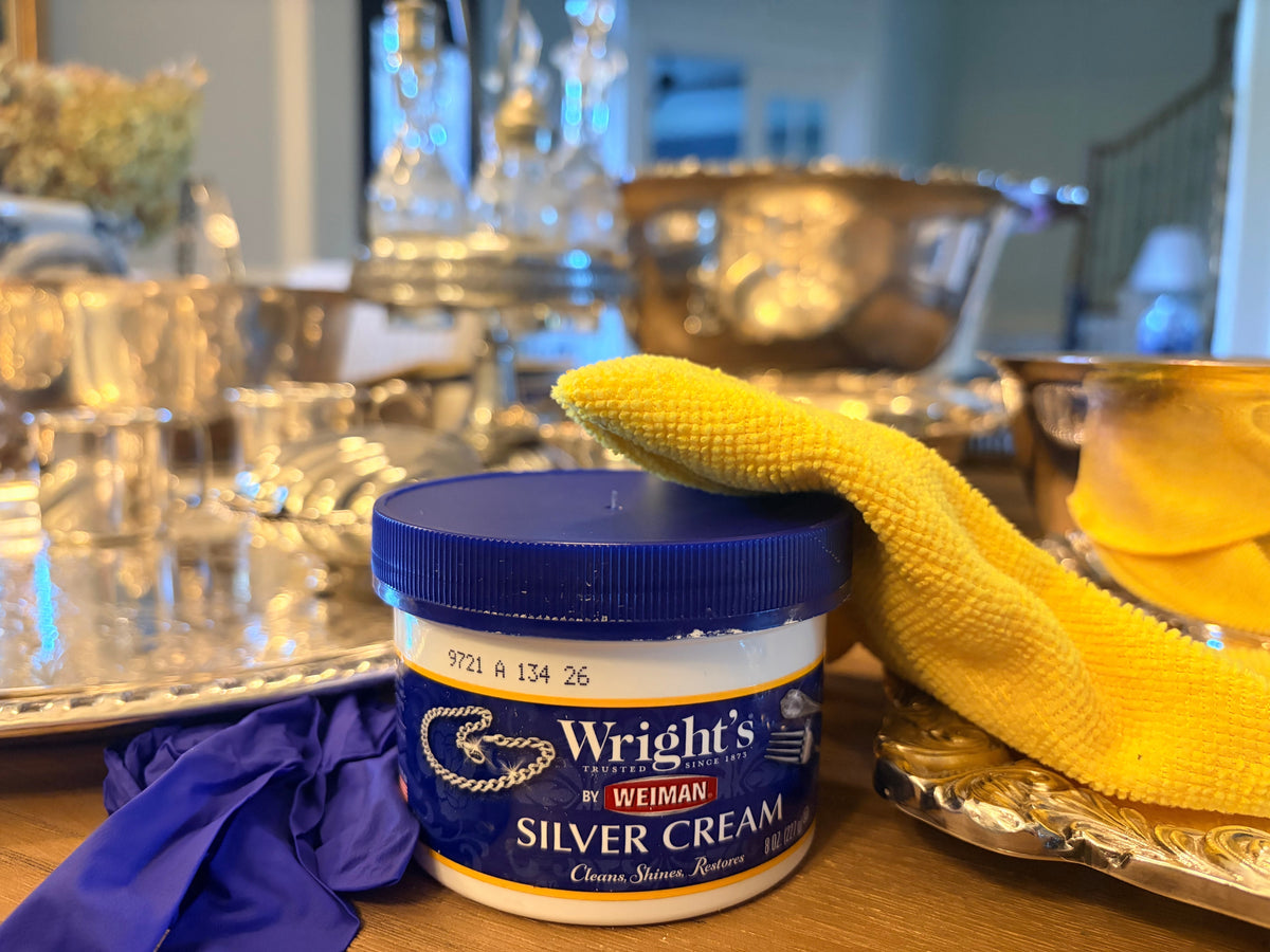 Jar of Wright's Silver Cream with a polishing cloth and nitrile gloves, with vintage silver pieces in the background