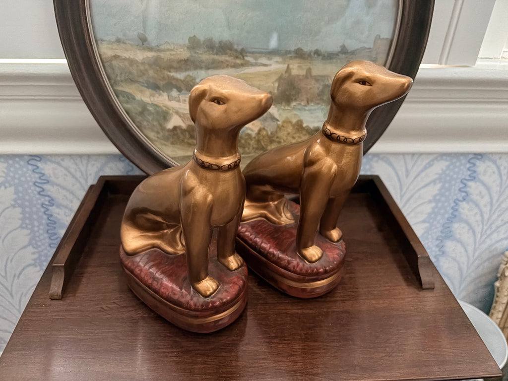 Pair of gold whippet figurines on red tufted cushions by Raymond Waites